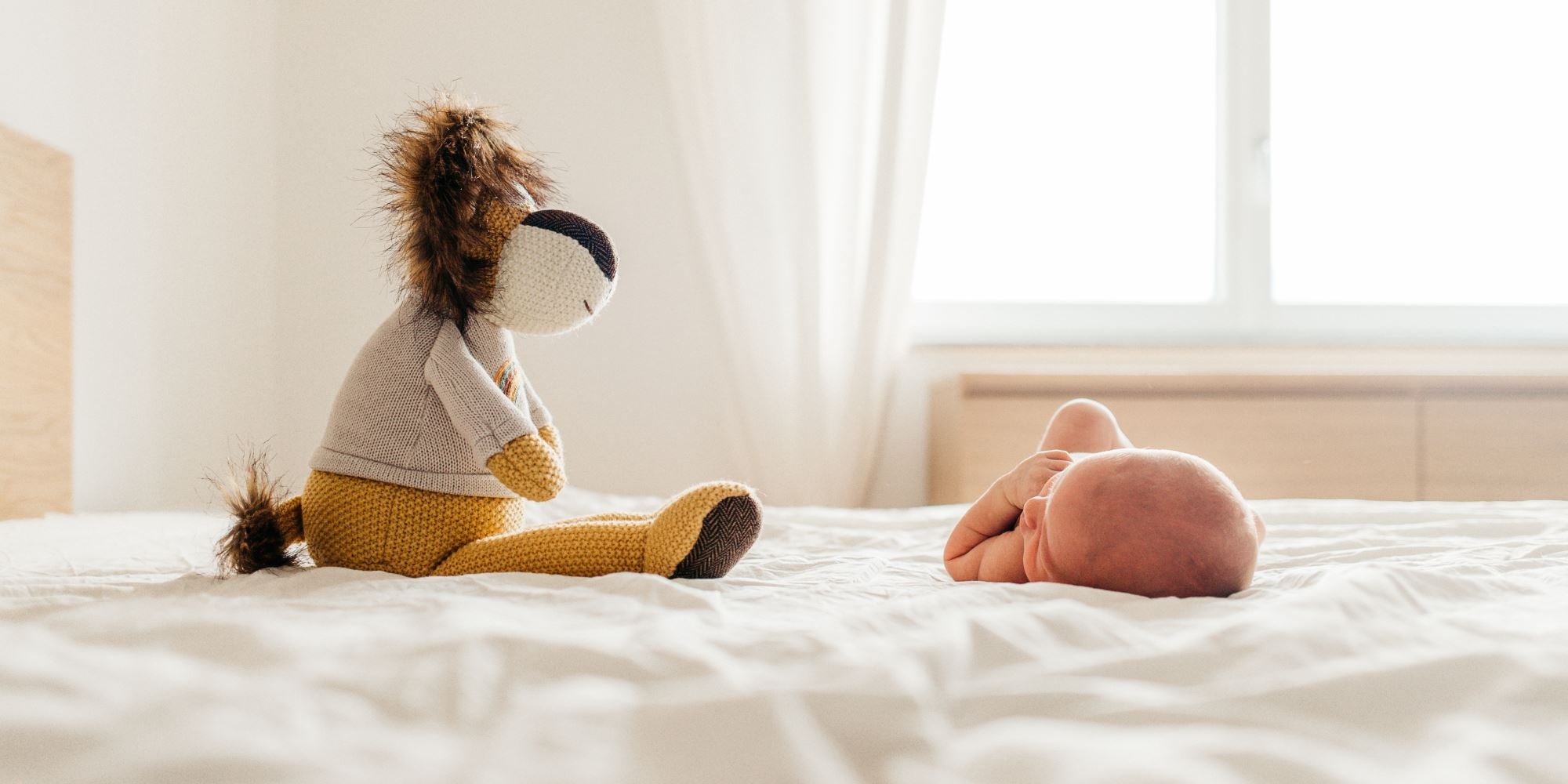 Baby auf einem Bett neben einem Stofftier. 