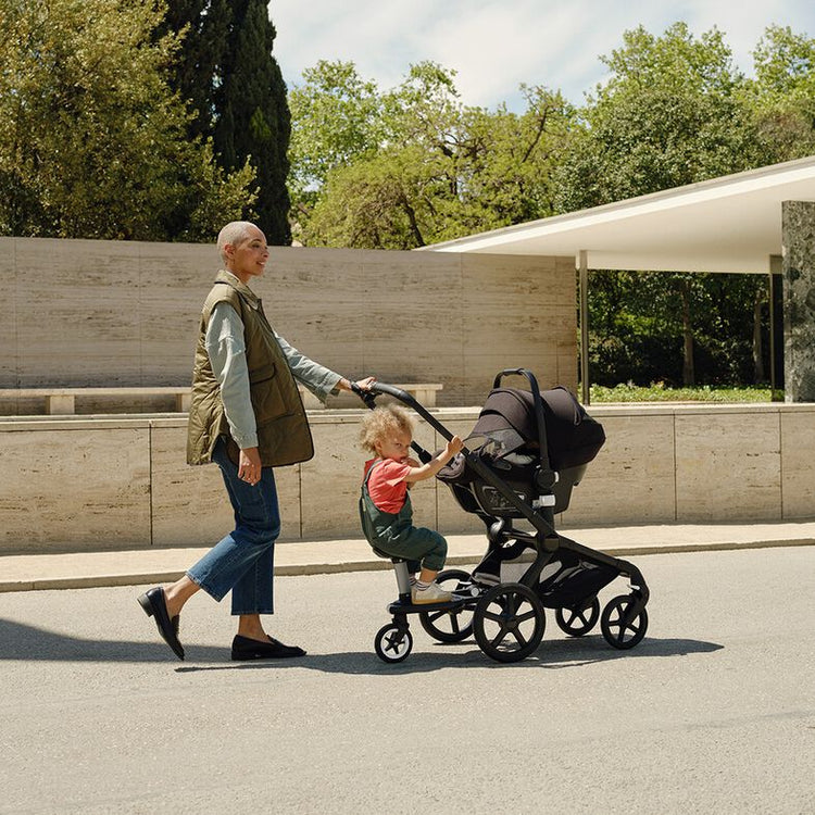 Frau mit einem Kinderwagen auf dem eine Babyschale draufgeklickt ist und ein Mitfahrbrett