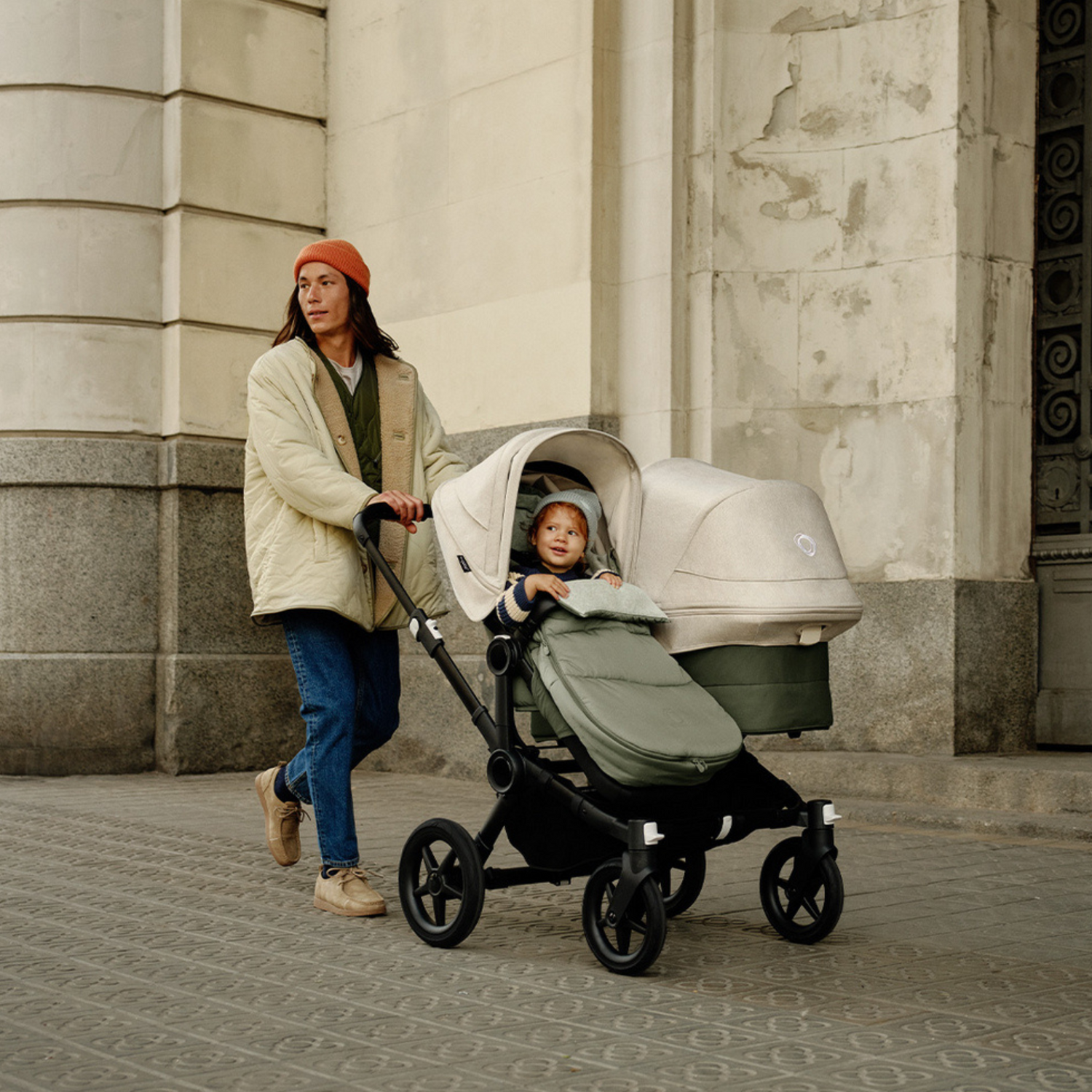 Mann mit einem Geschwisterkinderwagen mit beigen Sonnendächern. 