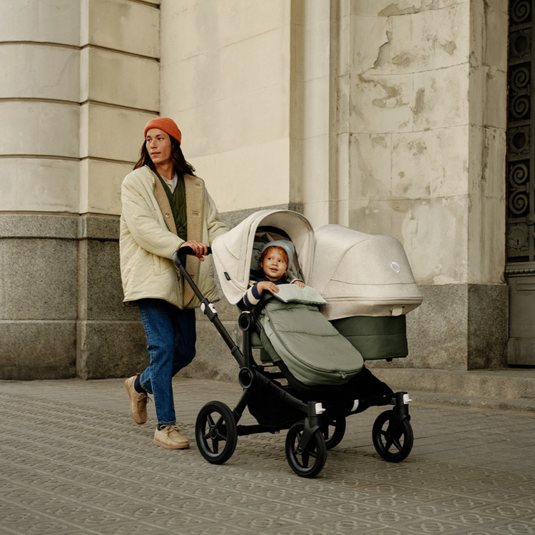 Mann mit einem Geschwisterkinderwagen mit beigen Sonnendächern. 