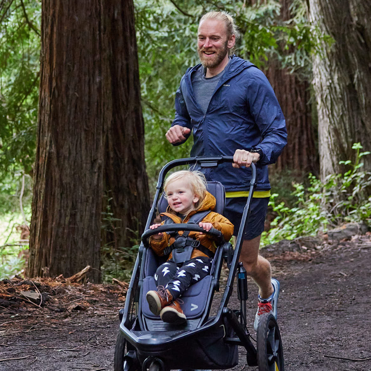 Mann lauft mit Sportkinderwagen im Wald