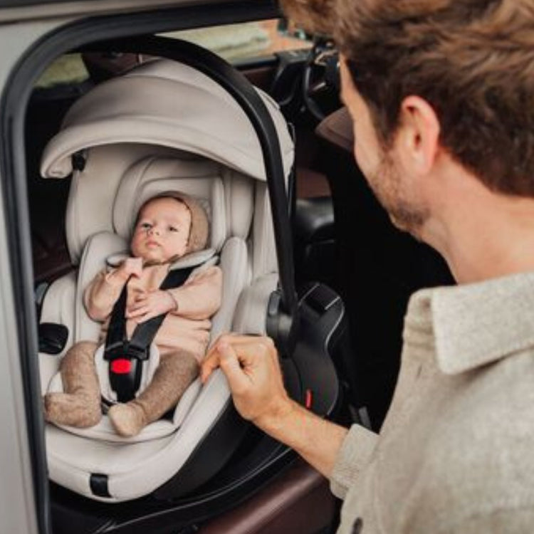 Mann von hinten schaut in sein Auto wo sein Baby in einer Babyschale liegt