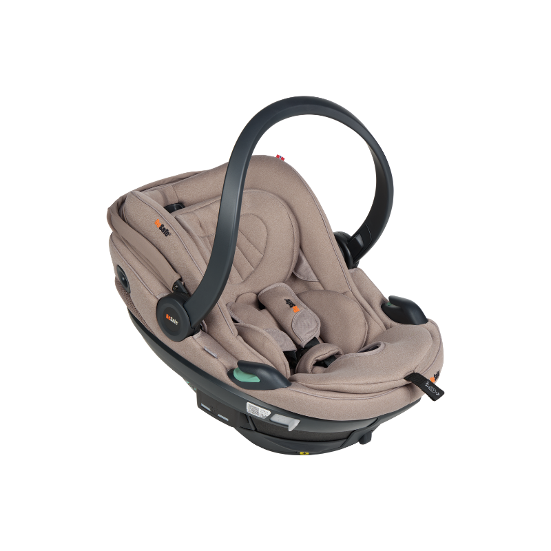 Beige Babyschale mit Tragegriff, gepolsterter Liegefläche und integriertem Gurtsystem in schräger Seitenansicht.