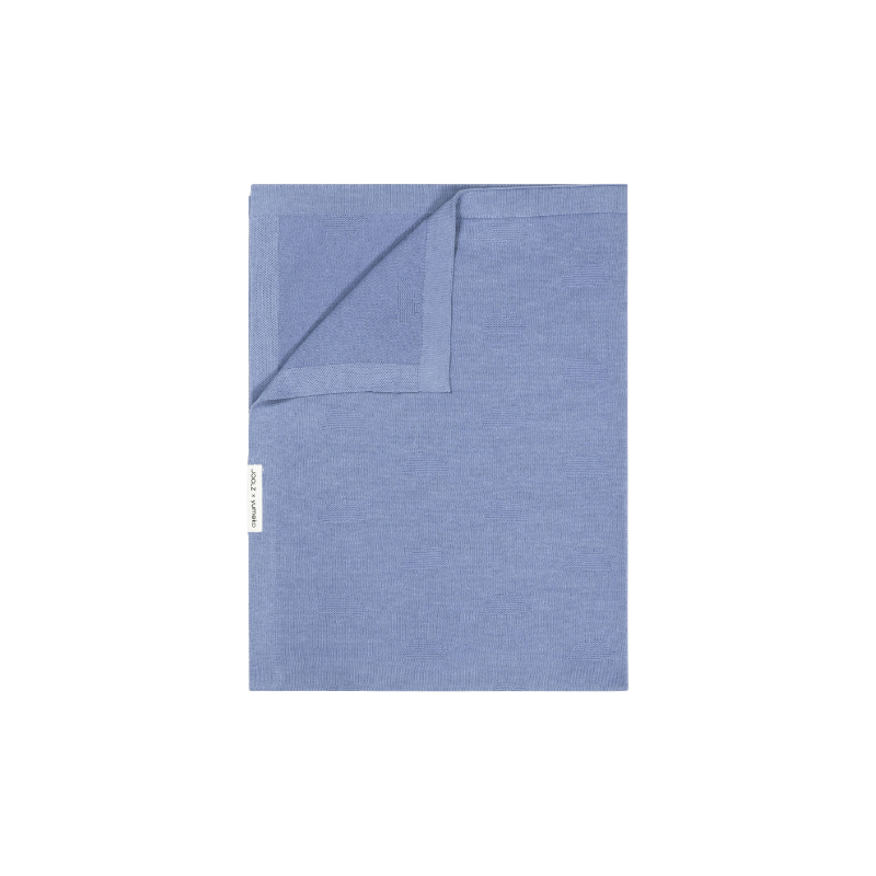 echteckige Decke aus Stoff in hellblaue Farbe, eine Ecke leicht umgeschlagen, mit kleinem seitlichem Etikett.