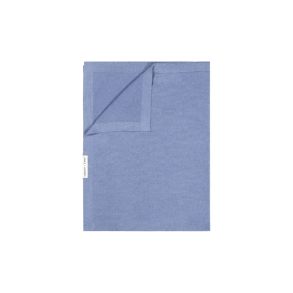 echteckige Decke aus Stoff in hellblaue Farbe, eine Ecke leicht umgeschlagen, mit kleinem seitlichem Etikett.