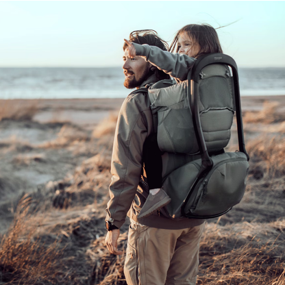 Thule Kindertrage beim Wandern am Meer – Vater trägt Kind in ergonomischer Rückentrage in Grün, ideal für Outdoor-Abenteuer und Familienwanderungen
