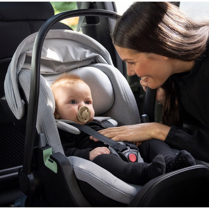 Thule Babyschale im Auto – Mutter sichert ihr Baby in einer grauen Thule Babyschale mit ISOFIX-Basis, gepolsterter 5-Punkt-Gurt für maximale Sicherheit