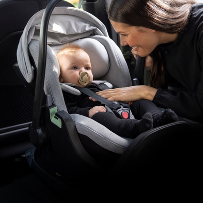 Thule Babyschale im Auto – Mutter sichert ihr Baby in einer grauen Thule Babyschale mit ISOFIX-Basis, gepolsterter 5-Punkt-Gurt für maximale Sicherheit