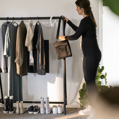 Frau hängt eine schwarze Thule Tasche mit Schultergurt an eine Kleiderstange neben Jacken und Schuhen